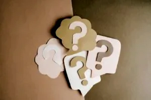 Question mark cutouts in layered paper craft style on a brown backdrop, conceptual art.